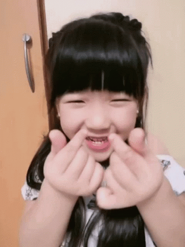 a young asian girl holding her hands together to put their faces to the camera