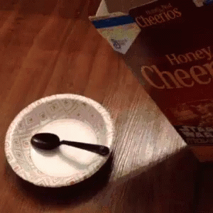 a bowl of cereal, a book and spoon on a table