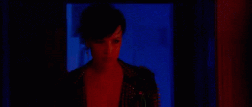 a woman standing in a doorway with a black jacket and blue light shining in her