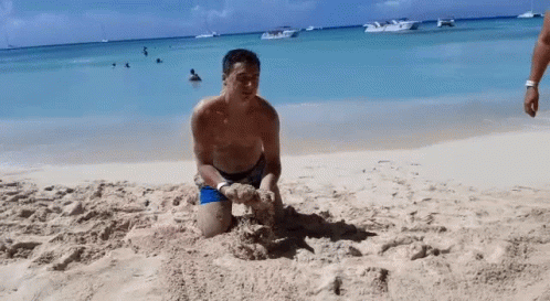 a young man in a blue suit plays with his sandcastle