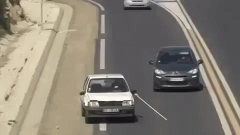two cars are driving down the highway, one is white