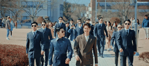 a group of men in suits walking on the sidewalk