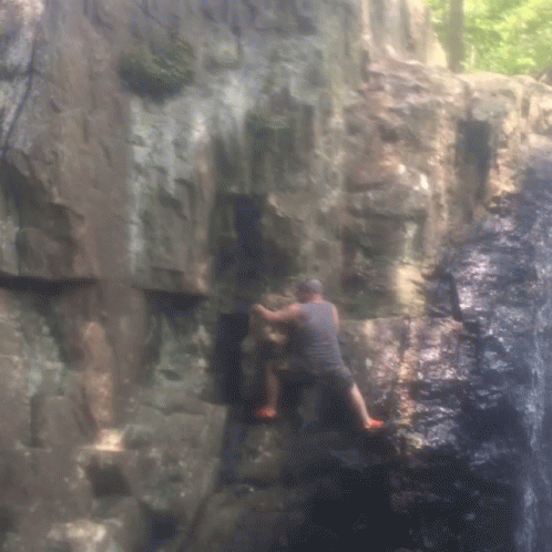 a man climbing on rocks and rock walls with water