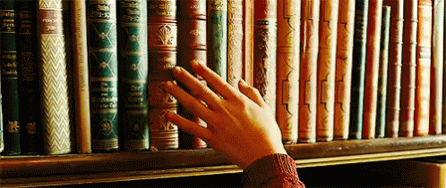 a hand reaching for a book in front of a bookshelf