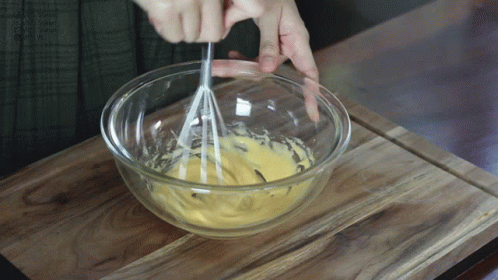 hands whisk blue batter into a bowl with a metal spoon
