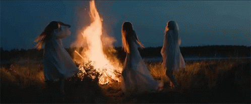 three women standing around a flame in a field