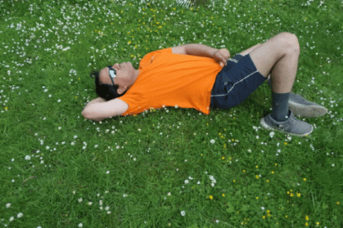 a person laying in the grass while wearing a blue shirt
