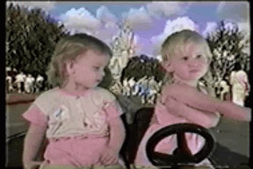 a couple of small girls holding onto the handle of a car steering wheel