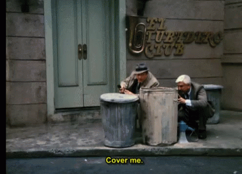 two men are sitting next to trash cans in front of a building