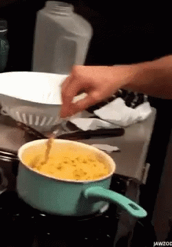 a person cooking soing on a stove while another person puts a pot in it