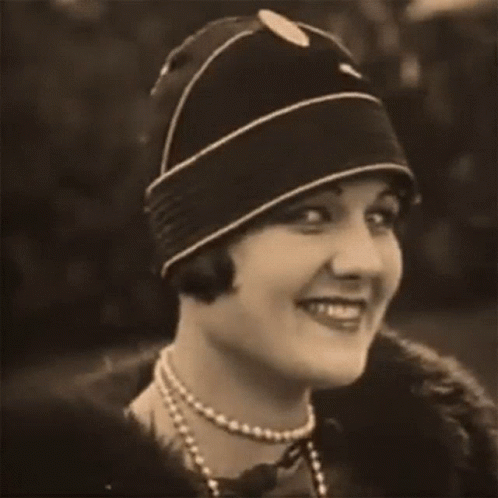 a woman in a hat smiles while wearing pearls