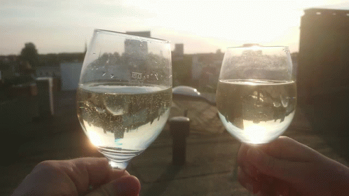 two hands holding wine glasses near a view of a town