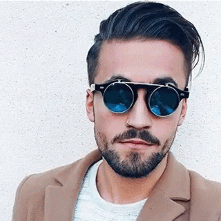 a man with glasses and beard is in front of a white wall