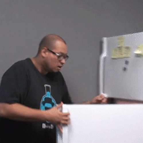 a man wearing glasses opening a refrigerator door