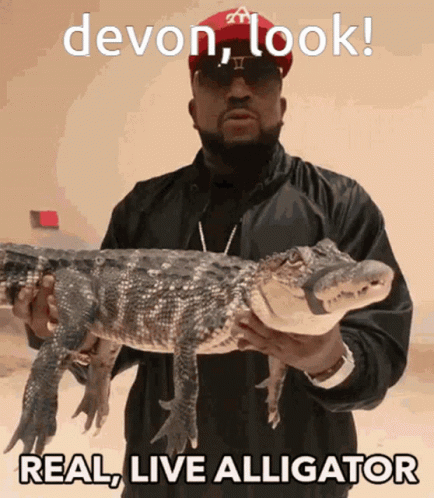 a man with glasses is holding a large alligator