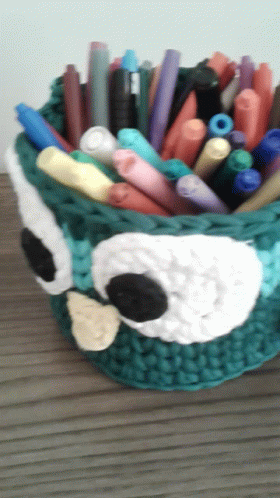 a crochet basket with pens and crayons in it