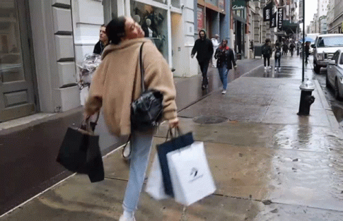 woman in blue sweatshirt walking down street carrying shopping bags