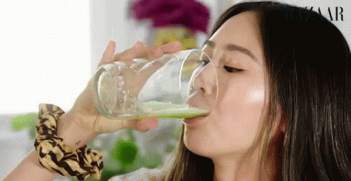 a woman drinking from a glass with green liquid