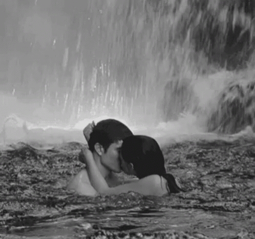 black and white pograph of a woman kissing a man in the water