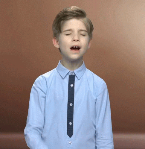 a boy in a tan shirt has his eyes closed and a tie around his neck
