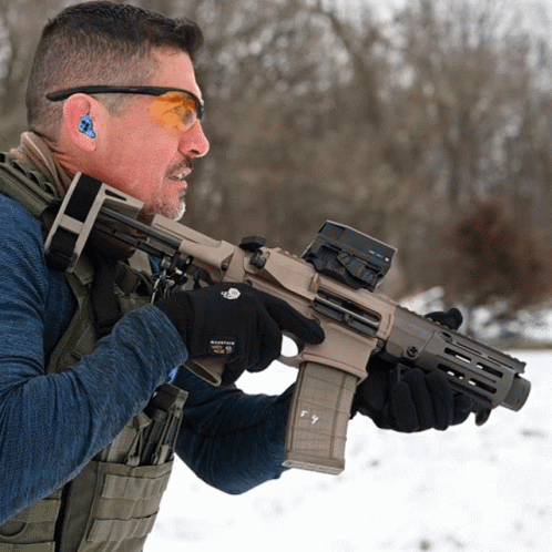 a man holding an automatic rifle while wearing goggles