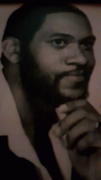 black man with beard is holding a phone up to his ear