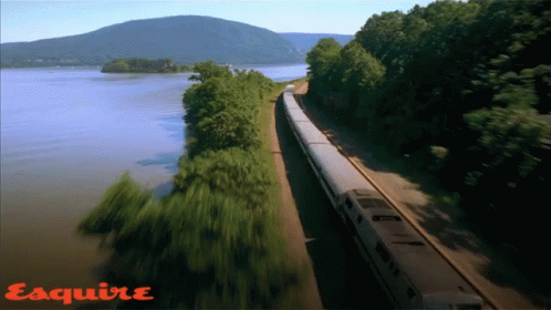 a train traveling down tracks near a river and some mountains