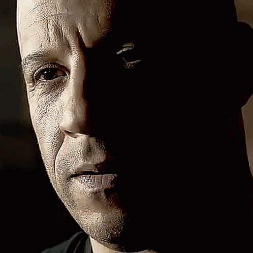 a bald man in dark colors looks to the side