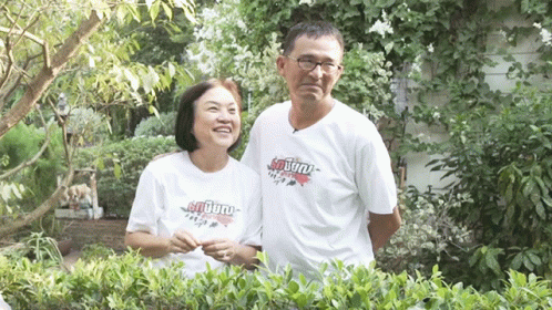 man and woman wearing shirts standing near a bush