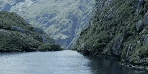 a person is wading in a river with cliffs