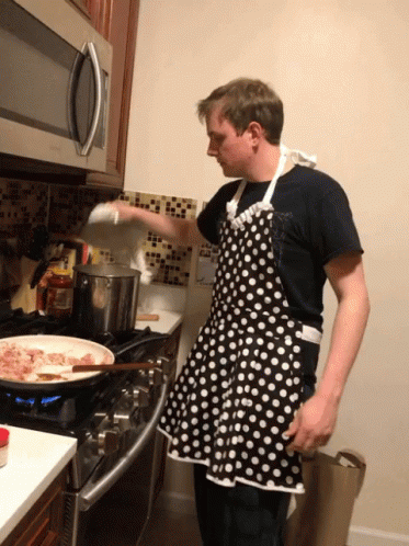 man in apron cooking a large pan with food on it