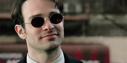 a man wearing sunglasses and a suit looks at the camera