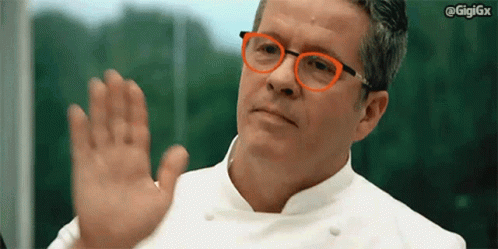 a man with glasses and a white chef shirt holds out his hand while gesturing