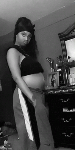 a pregnant woman wearing a halter top is standing by a dresser