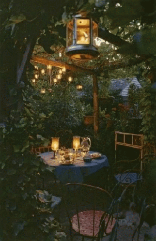 an outdoor dinner setting with lanterns hanging over the table