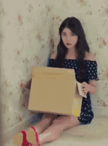 a girl in a black dress holding an open box sitting on her bed