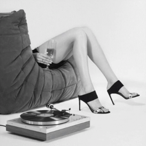 a woman in black high heels is holding a glass of wine and vinyl record