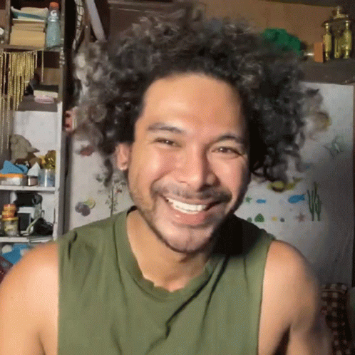 a man wearing an olive colored tank top smiles for the camera