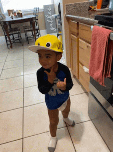 a little boy standing in the kitchen wearing a blue hat