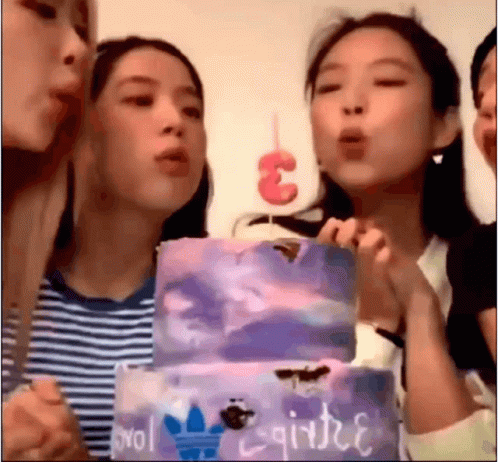 three young ladies blowing out candles on a large cake