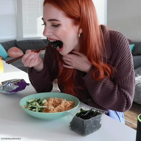 a girl with blue hair, wearing a black sweater, eating soing off a spoon