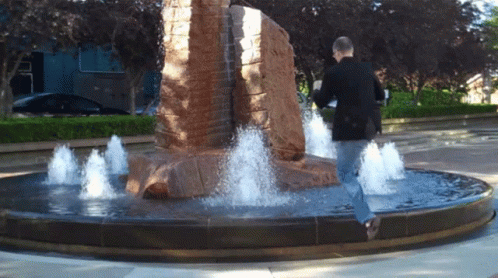 a large water fountain with a man walking in the distance