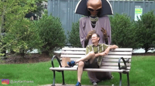 a person sitting on top of a bench with an alien statue