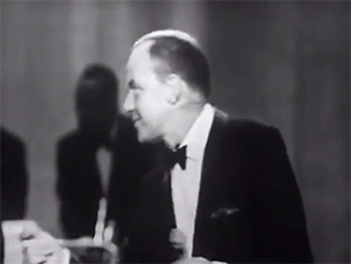 a man sitting at a table laughing while wearing a suit and tie