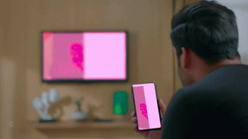 a person standing in front of a flat screen tv holding up a phone