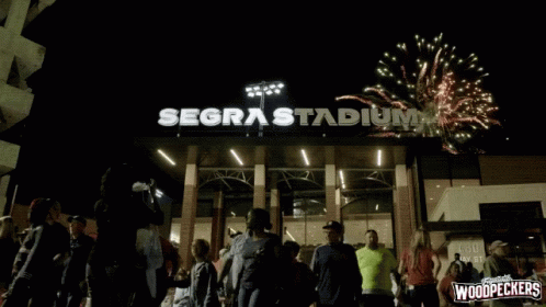 people stand outside of a stadium with fireworks