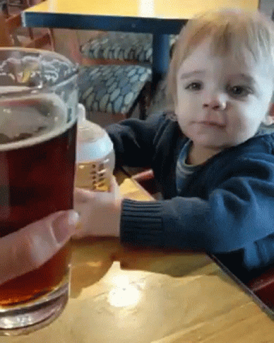 a young child sitting at a table next to a large glass of beer