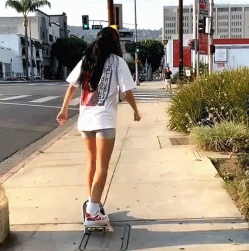 a woman skateboards down the sidewalk on a city street
