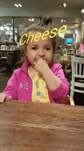 a little girl sitting at a table with the word cheese written on it