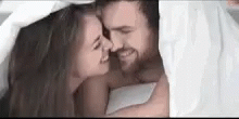 a woman and man are cuddling together under the covers